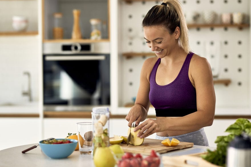 Happy athletic woman cutting fruit while preparing healthy meal in the kitchen.