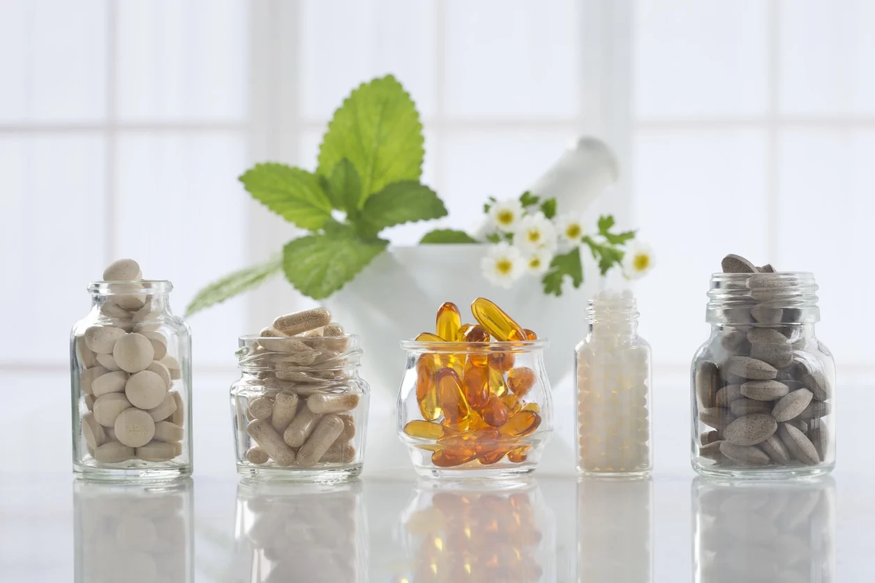 Five glass jars lined up on counter in front of window with different supplements in each