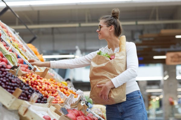 Woman at a fruit stand selecting produce while holding a brown paper bag full of fresh food