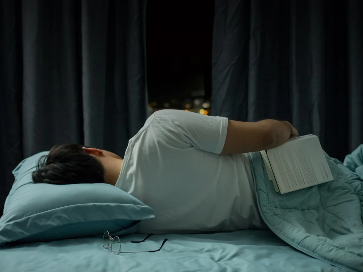 Person asleep in bed with glasses and a book