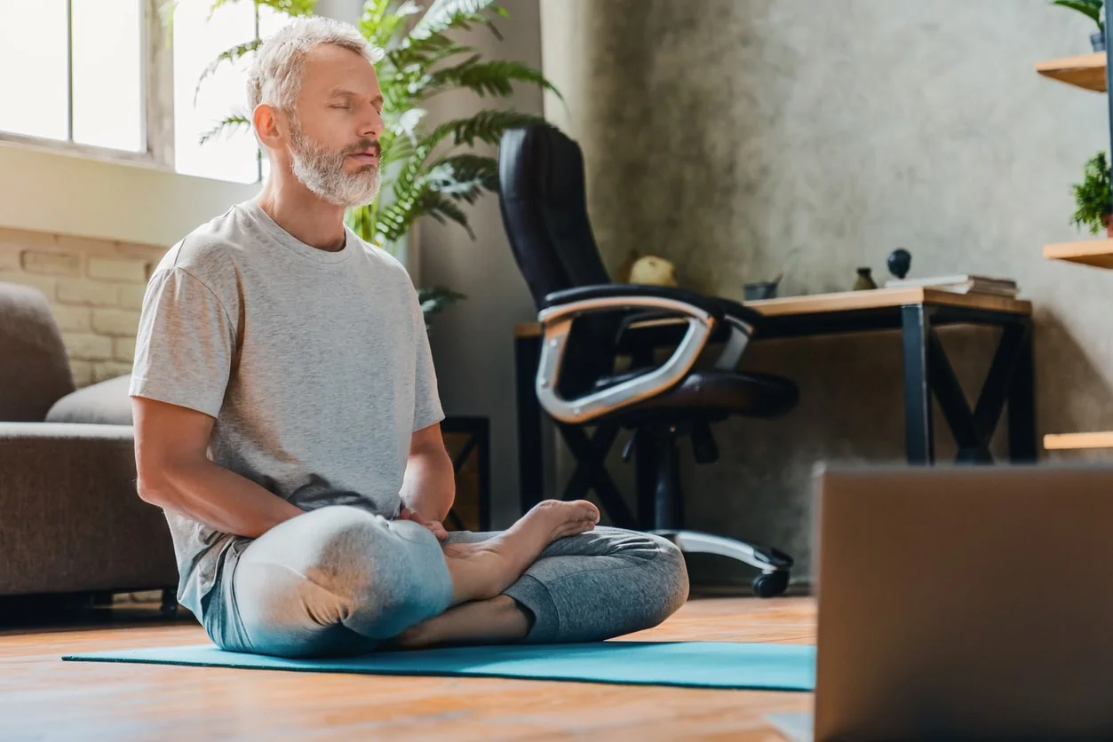 Middle aged man doing yoga and fitness at home using laptop
