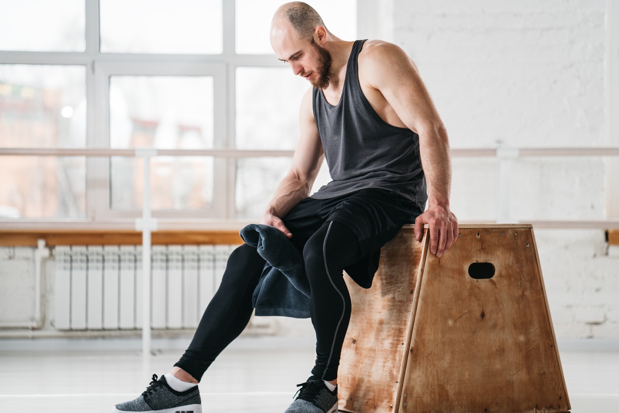 Sweaty muscular man sitting on box in a gym, resting after a hard workout.