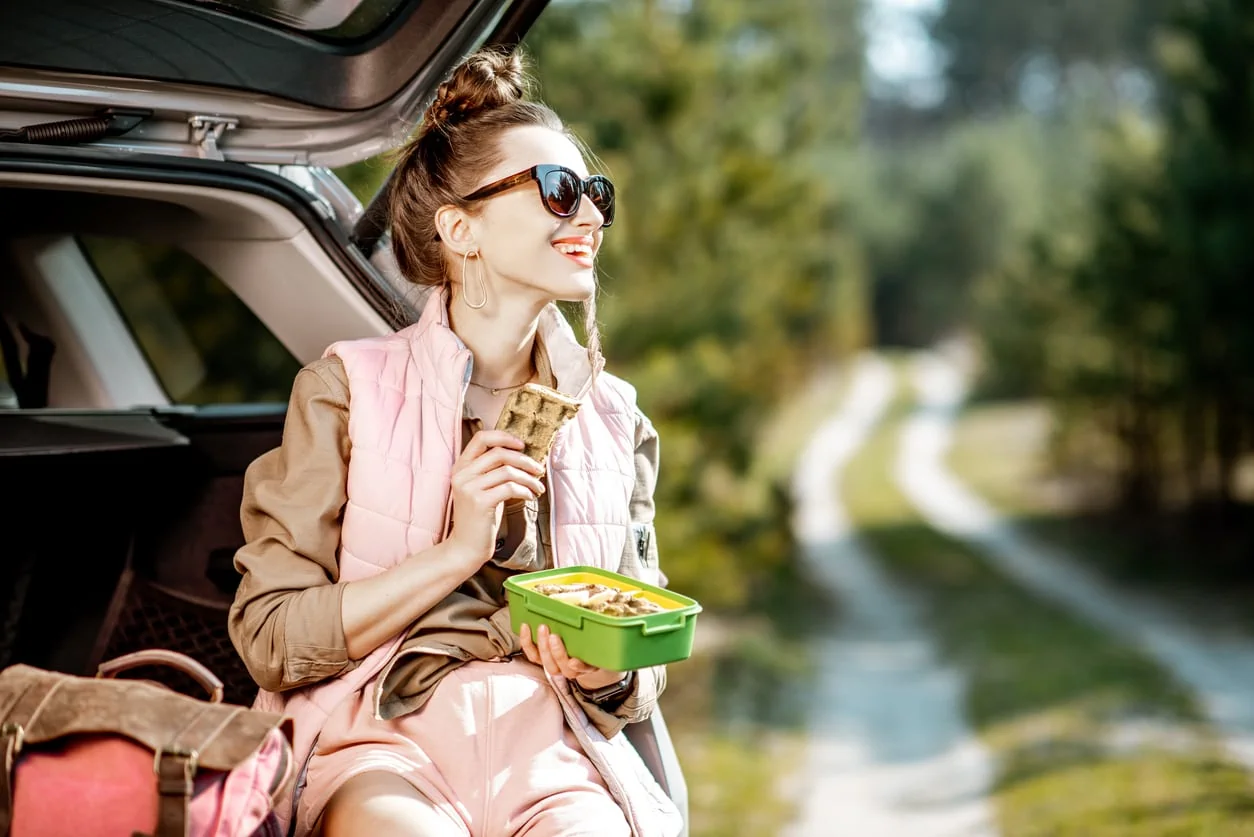 Young woman having a snack with lunch box while tarveling by car on vacation