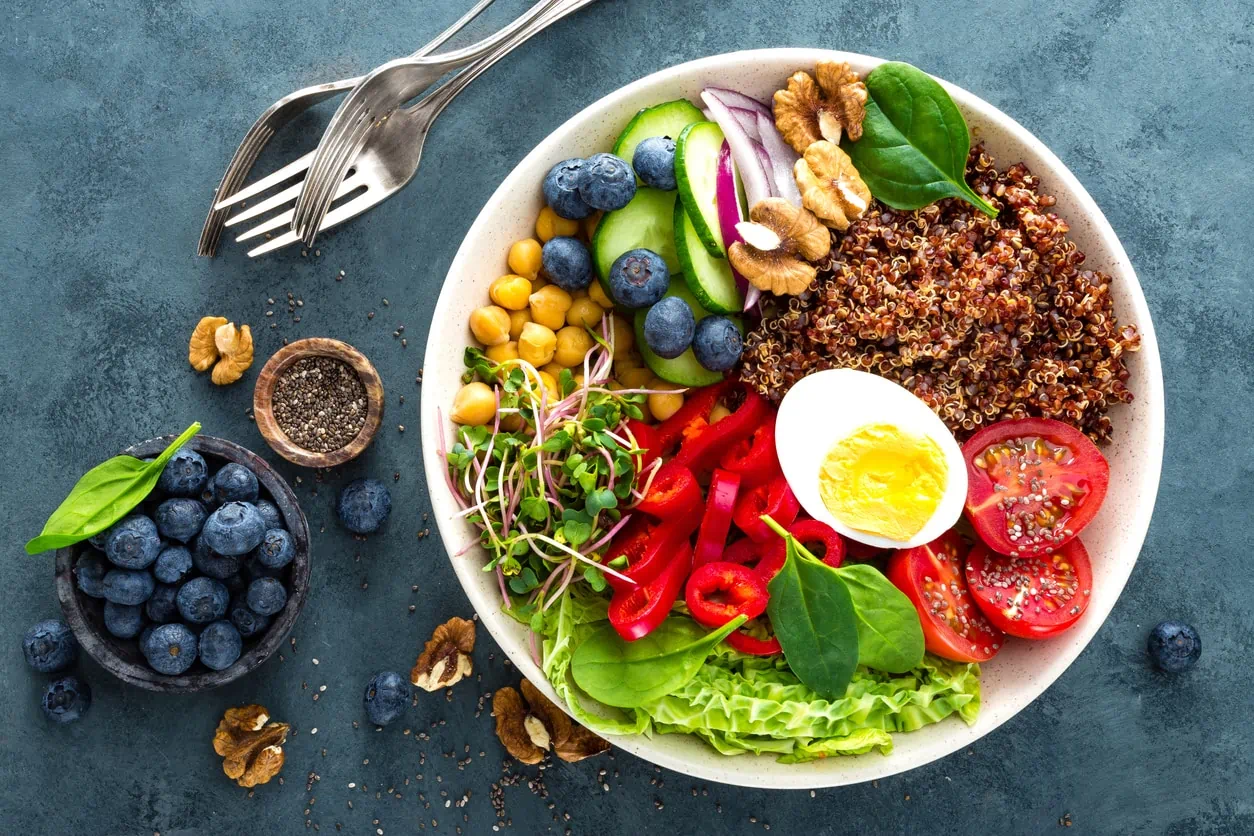 Buddha bowl dinner with boiled egg, chickpea, fresh tomato, sweet pepper, cucumber, savoy cabbage, red onion, green sprouts, spinach leaves, blueberry, walnuts, chia and quinoa. Healthy dish, lunch bowl. Detox diet. Balanced food. Top view