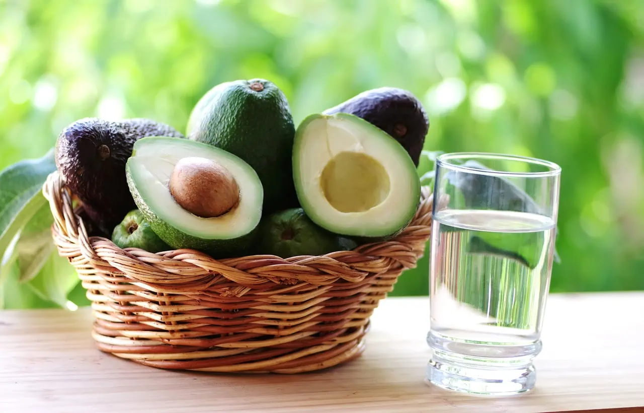 wooden basket full avocados fruit on a table with a glass of water next to it