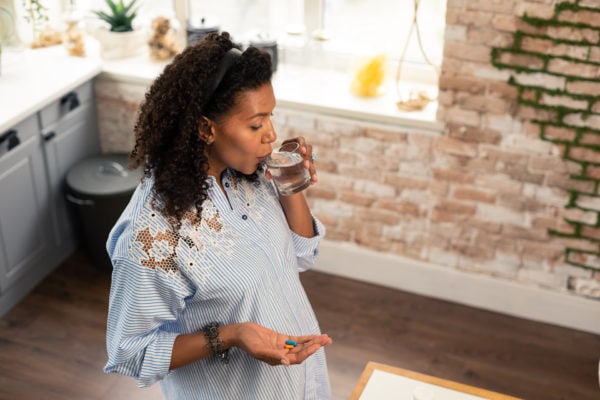 pregnant woman taking prenatal supplements with a glass of water