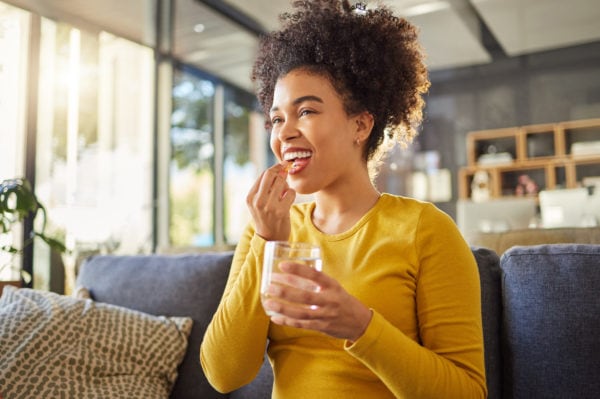 Young happy healthy woman taking an herbal supplement with a glass of water