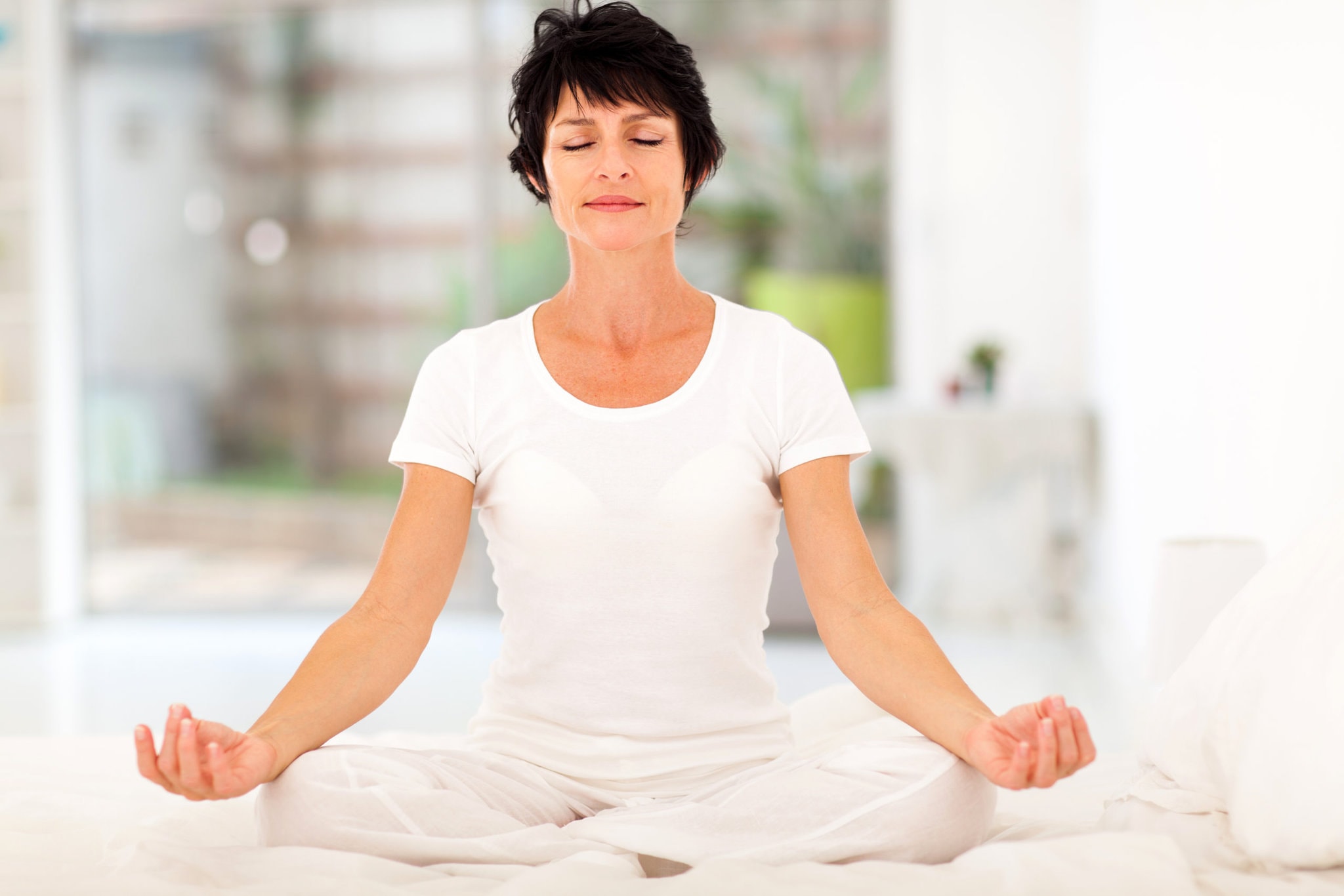 beautiful middle aged woman meditating on bed