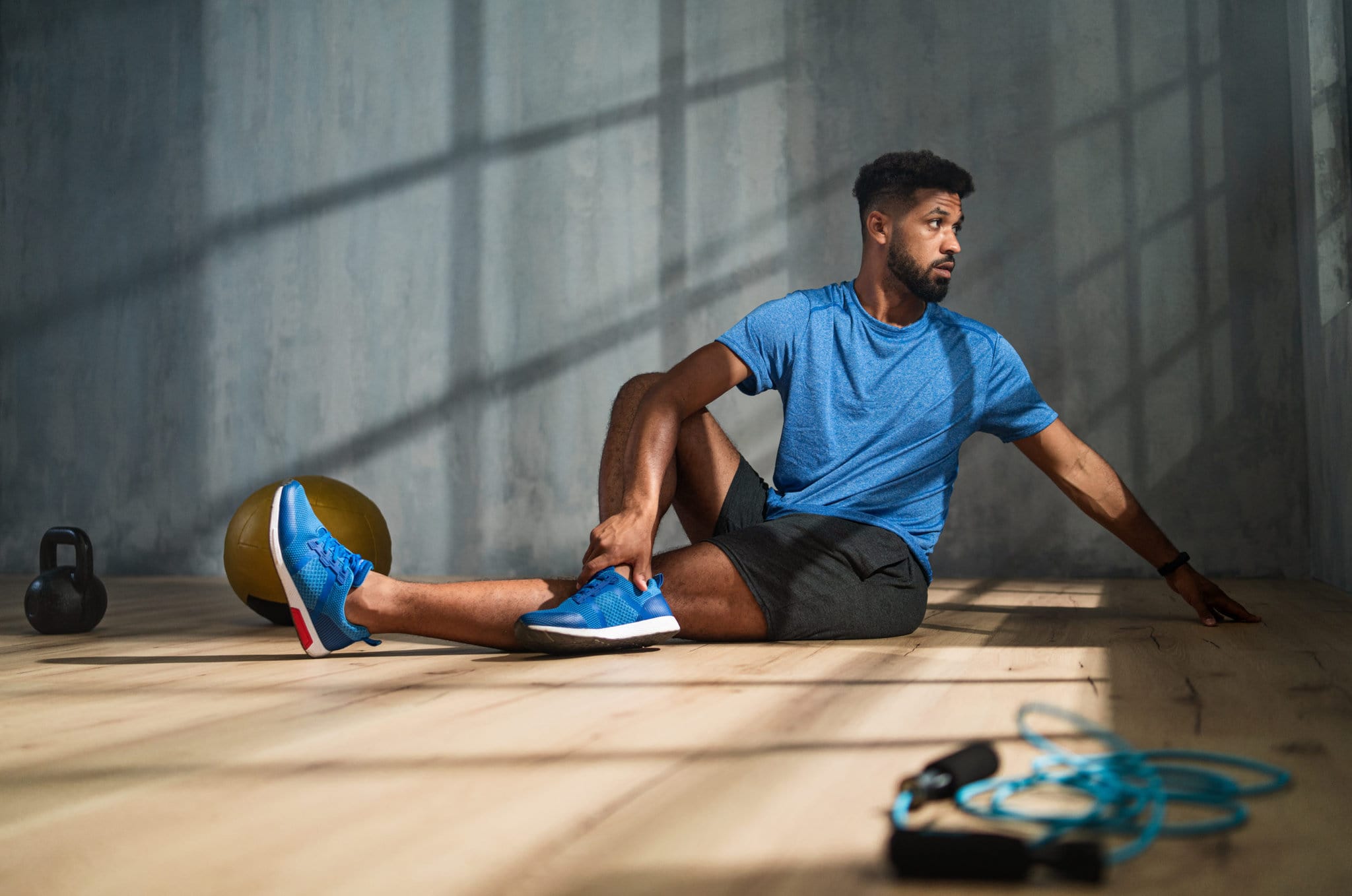 young athletic man sitting on gym floor stretching